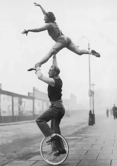 Framed Print : Male acrobat on unicycle supporting woman in air (B&W) Framed Print : Male acrobat on unicycle supporting woman in air (B&W)