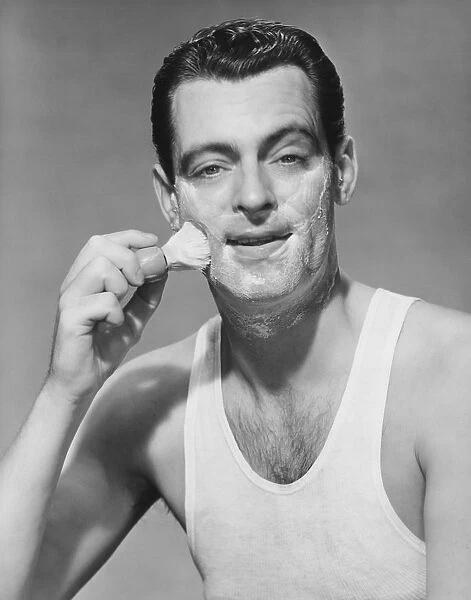 Man applying shave foam on face in studio, (B&W), portrait