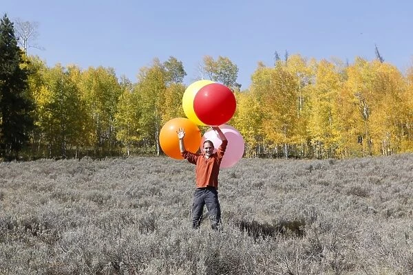 Man carrying huge balloons, landscape in fall, Utah, USA