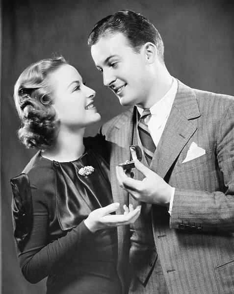 Man giving to fiance engagement ring in studio, (B&W), portrait