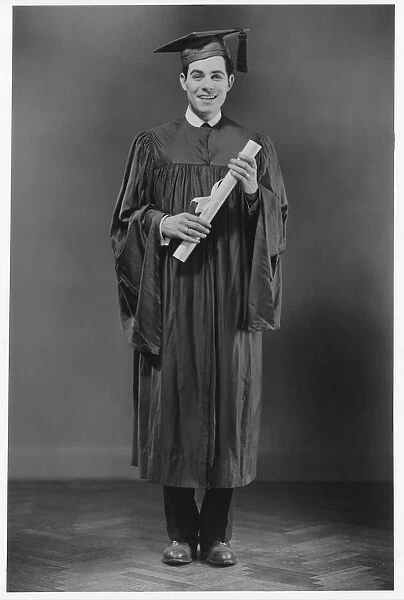 Man in graduation gown posing in studio, (B&W), portrait