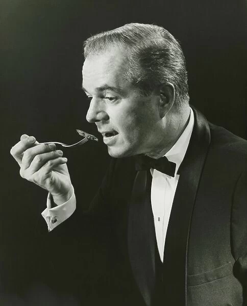 Man holding fork, taking bite in studio, (B&W), portrait