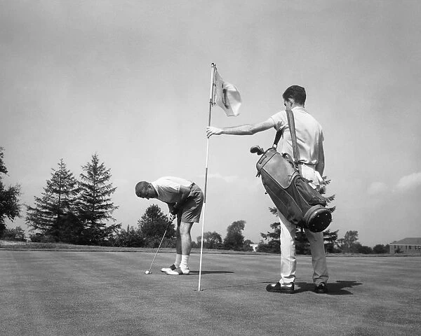 Man making golf shot while caddie stands holding flag