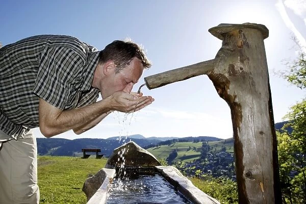 A man in his mid 40 quenches his thirst at a well, Todtnauberg in the Black Forest, Baden-Wuerttemberg, Germany, Europe