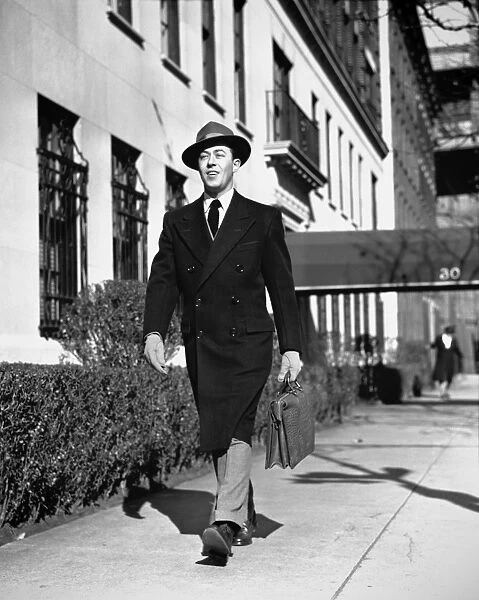 Man in overcoat walking on sidewalk, (B&W)