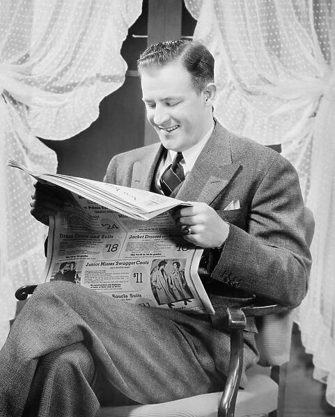 Man reading newspaper in living room, (B&W)