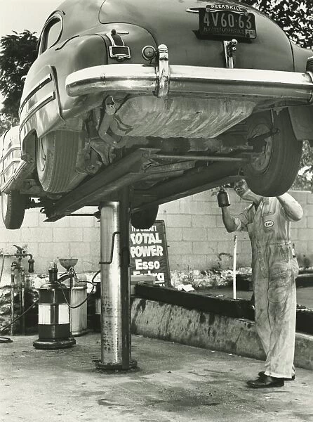 Man repairing uplifted car, (B&W), low section