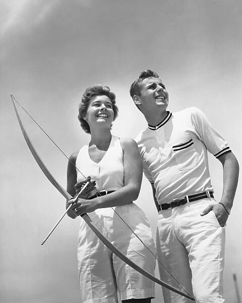Man standing beside woman who is holding bow and arrow