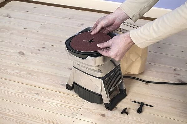 Man using hands to position circle of sand paper on edging sander