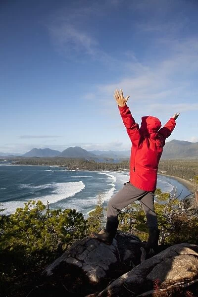 A Man Wearing A Red Jacket Looks Out At The View Of Cox Bay Near Tofino With Arms Raised; British Columbia Canada