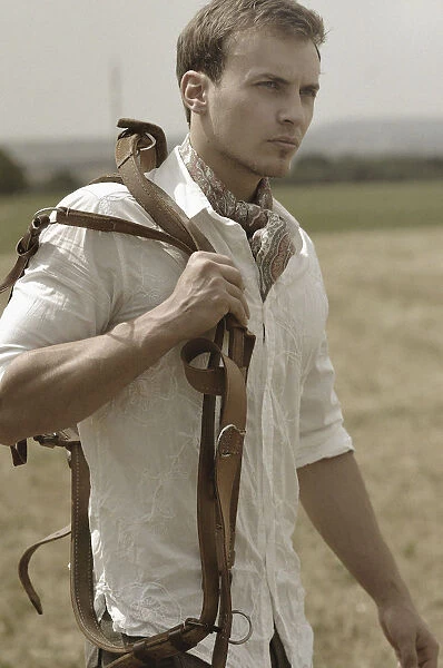 Man wearing riding clothes walking in a field in summer holding a leather strap