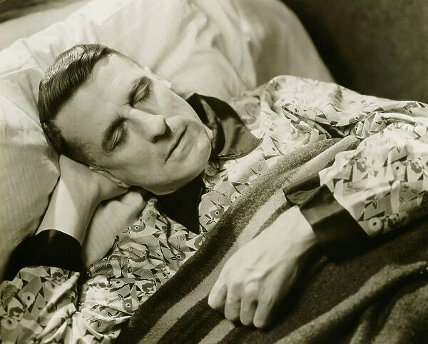 Man wearing silk pyjamas sleeping in bed, (B&W), elevated view