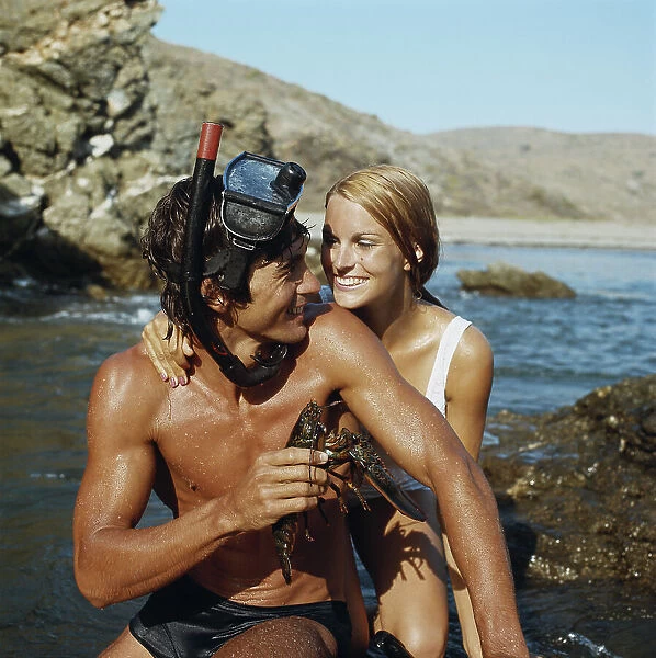 Man wearing snorkel, holding lobster beside woman, smiling