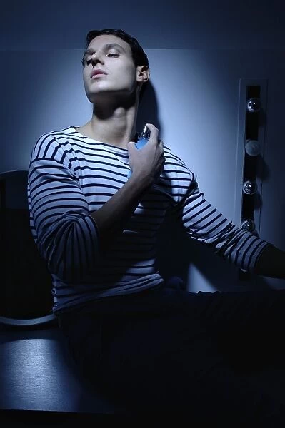 Man wearing a striped T-shirt in a bathroom, spraying on perfume