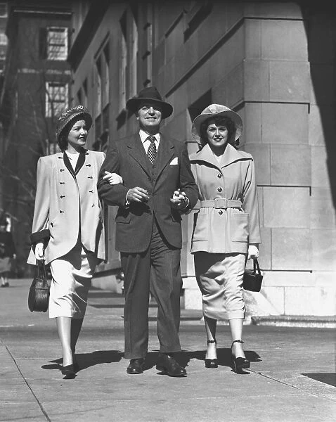 Man and two women walking on sidewalk, (B&W)