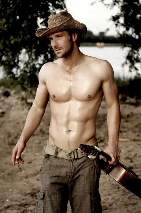 Framed Print : Masculine man without a shirt, wearing a cowboy hat and holding a guitar on a beach