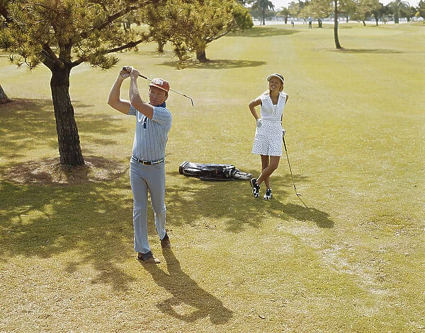 Mature couple playing golf, man swinging golf club