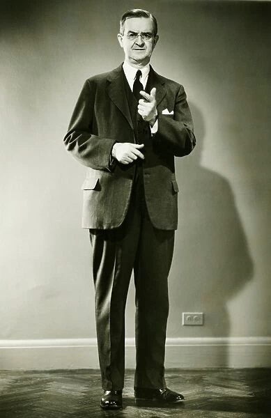 Mature man pointing in studio, (B&W), portrait