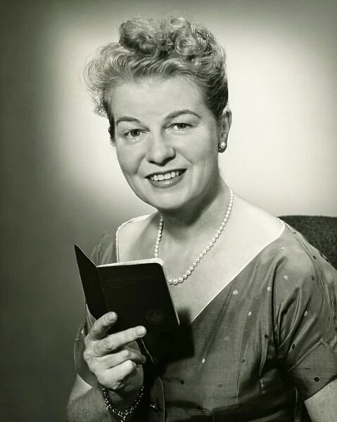 Mature woman holding small book, posing in studio, (B&W), portrait
