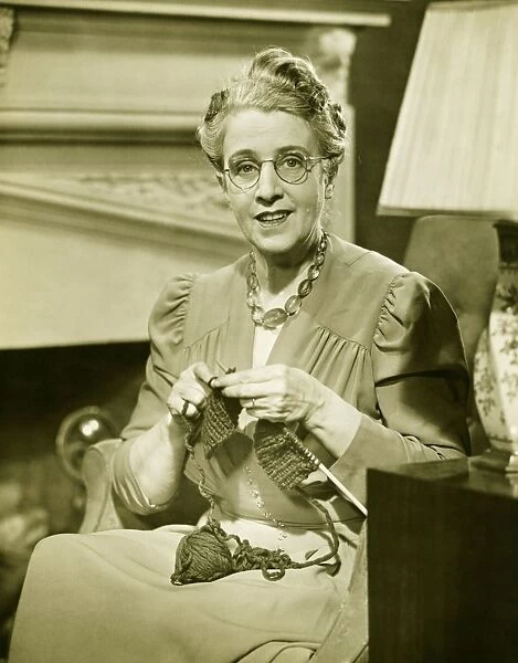 Mature woman knitting in living room, (B&W), portrait
