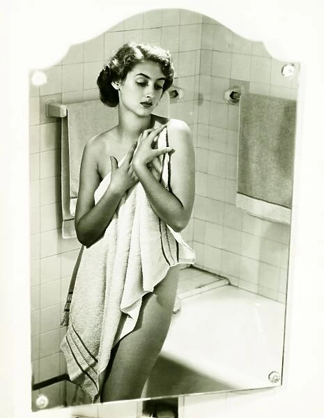 Mirror with reflection of woman covering herself with towel in bathroom, (B&W), portrait