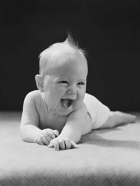 Five month old baby lying on stomach, arms outstretched, laughing