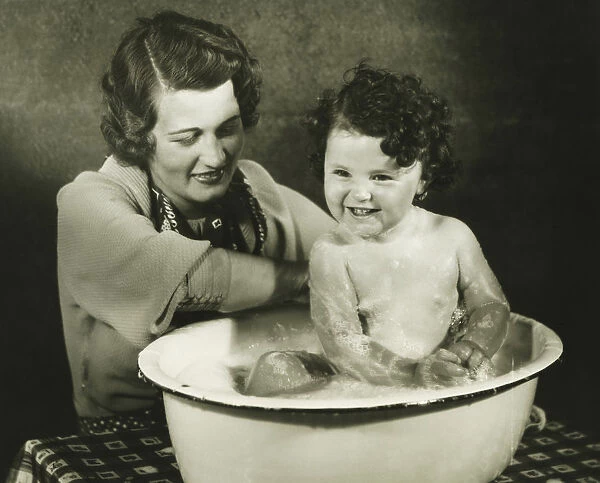 Mother bathing daughter (12-18 months) in basin, (B&W)