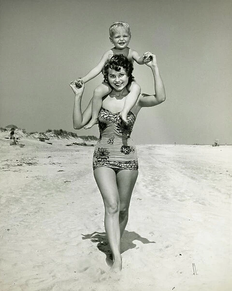 Mother carrying son (2-3) on shoulders, walking on beach, (B&W), portrait