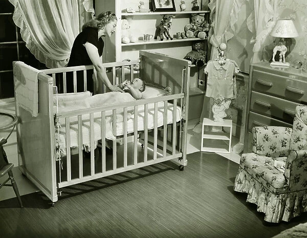 Mother looking at baby (3-6 months) lying in crib, (B&W)