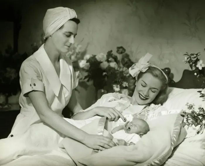 Framed Print : Mother lying in bed smiling to baby-child (0-6 months), nurse standing beside, (B&W)