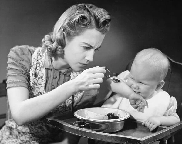 Mother trying to feed unwilling baby (9-12 months), (B&W)