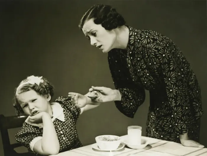Framed Print : Mother trying to make daughter (4-5) finish food at table, (B&W) Framed Print : Mother trying to make daughter (4-5) finish food at table, (B&W)