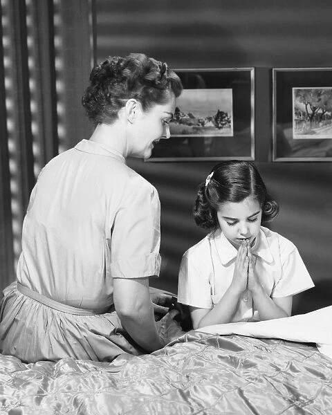 Mother watching daughter say bedtime prayers