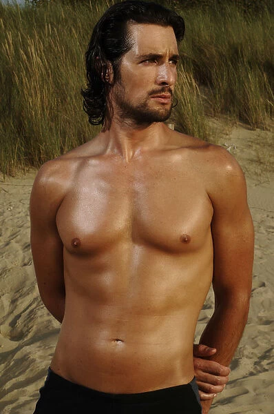 Muscular man wearing swimming trunks standing on a beach