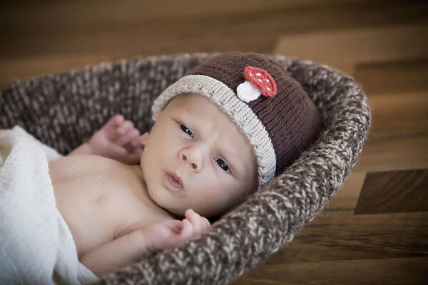 Newborn baby, 3 weeks, wearing a hat, lying in a basket