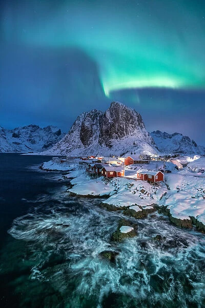 Northern lights over snowcapped mountain, village and dramatic sea in Hamnoy