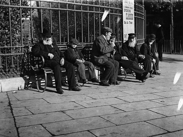 Old Men. circa 1900: A young boy sits on a bench next to a group of old