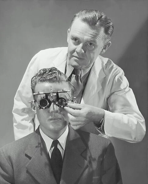 Optometrist giving man eye examination (B&W)