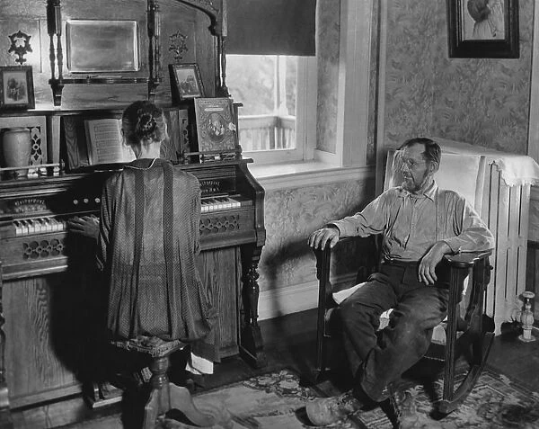 Organ Music. A man sits in an armchair listening to a woman as she plays the organ