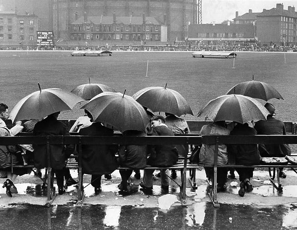 Oval Rain. circa 1946: A group of spectators sit underneath umbrellas in the rain