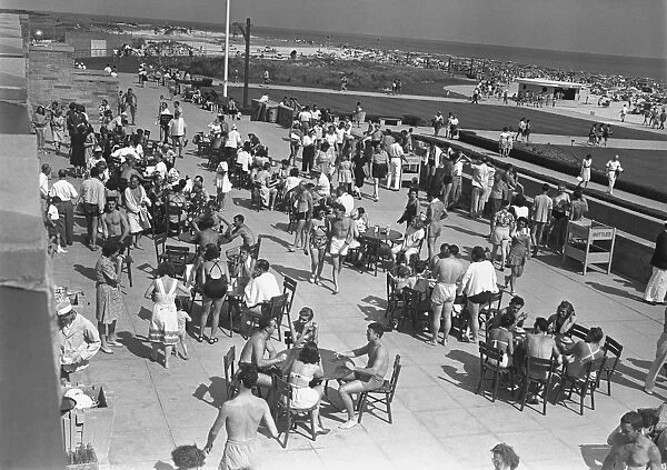 People sitting at tables by beach, (B&W), elevated view