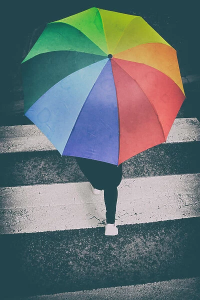 Person crossing a pedestrian crossing with a rainbow umbrella