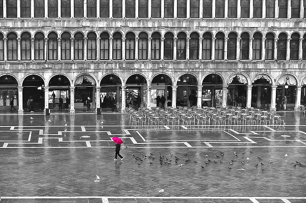 One person with a red umbrella crossing the St Marks Square by a rainy day in winter in Venice, Italy