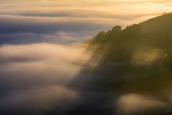 Peveril Castle shadows above the golden fog at sunrise. English Peak District. UK