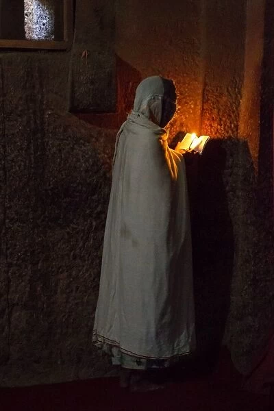 Prayers. A woman reads the bible under the light of a candle in Bet Medhane