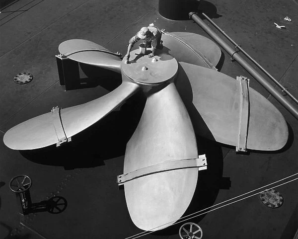 Propeller. A man painting a huge ships propeller, circa 1950