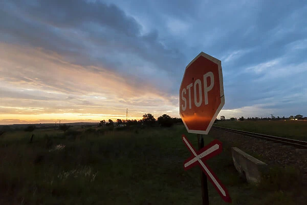 Railway crossing warning signal with Stop sign at sunset near the town of Magaliesburg, Gauteng Province, South Africa