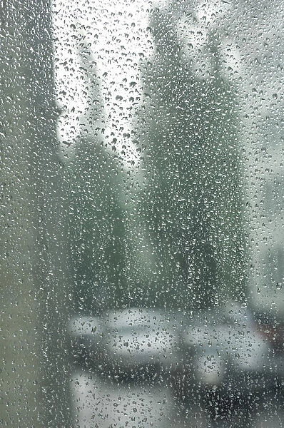 Rain drops on a window pane, blurry buildings and cars in the back