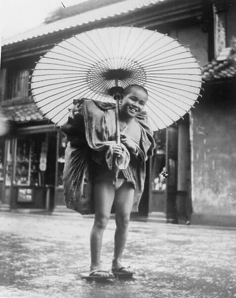 Rainy Day. circa 1930: A Japanese boy hoists up his kimono to protect it