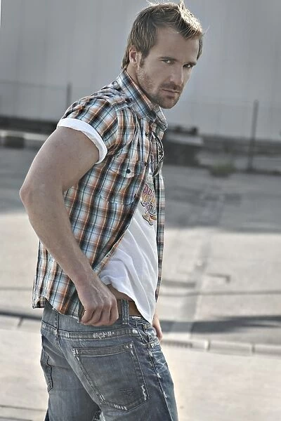 Rebellious man wearing jeans and a plaid shirt at a gas station, turning round